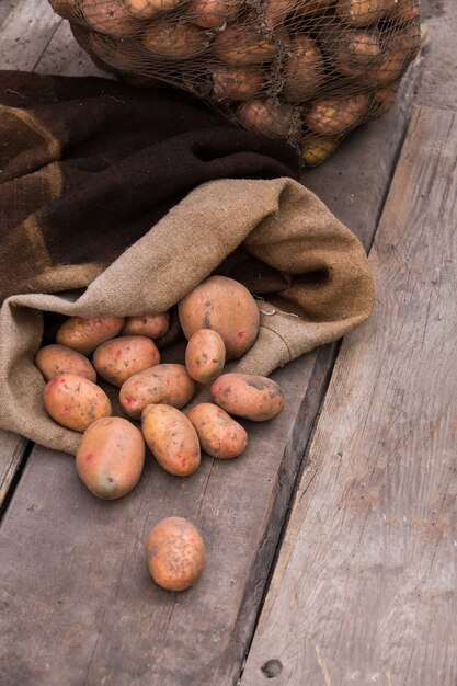 Frisch geerntete Kartoffeln mit Erde noch auf der Haut, die aus einem Leinensack auf einer rauen Holzpalette verschüttet wird.