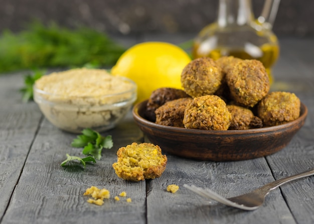 Frisch gekochte Falafel auf Tonschale auf einem Holztisch mit Tahinisauce und Öl