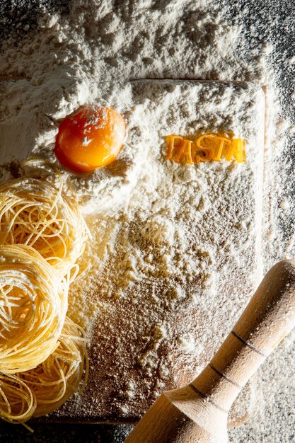 Frisch gekochte Nudeln liegen auf einer dunklen Oberfläche, die mit Mehl bestäubt ist. Italienische Pasta. Tagliatelle. Rohe Nudeln. Italienisches Nudelrezept. Draufsicht, Kopierraum.