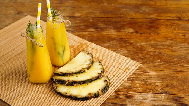 Frisch gemachter Ananassaft mit Eis in einer kleinen Glasflasche auf Holzhintergrund. Hausgemachtes Getränk.