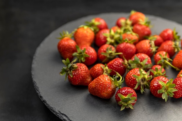 Frisch gepflückte Bio-Erdbeeren der Bauern auf grauer Platte. Reife Erdbeeren mit grünen Stecklingen.