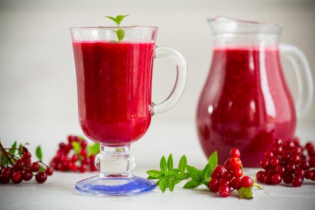 Frisch gepresster dicker natürlicher Saft mit Fruchtfleisch aus reifem rotem Viburnum in einer Karaffe auf einem Holztisch