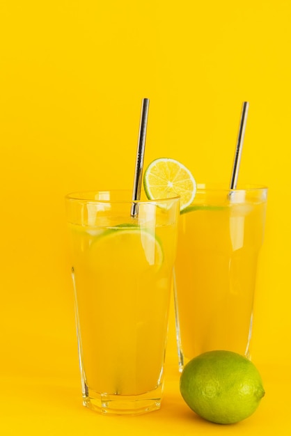 Frisch gepresster Orangensaft mit Eis und Limettenscheiben in Gläsern auf gelbem Hintergrund