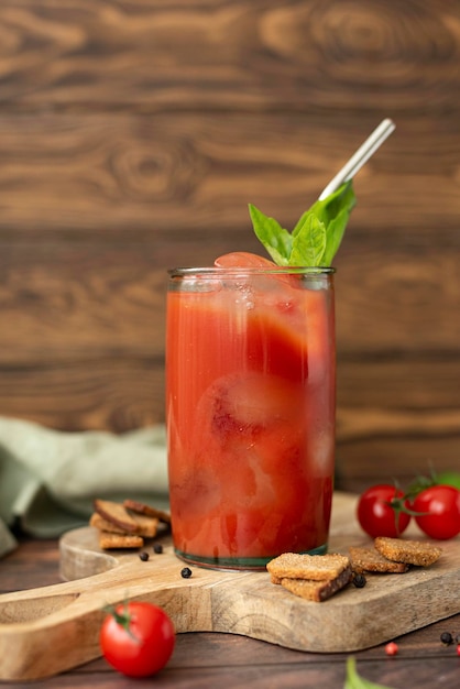 Frisch gepresster Tomatensaft mit Basilikum und Croutons in einem Glas auf einem Holztisch