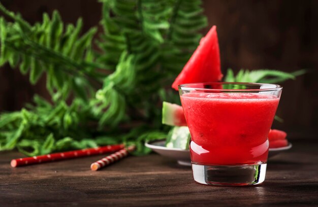 Frisch gepresster Wassermelonen-Smoothie im Glas und Wassermelonenscheiben auf altem hölzernem Küchentischhintergrund