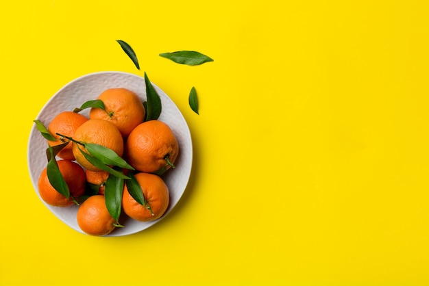 Frisch geschnittene Clementinen und ganze Mandarinen über runder Platte auf farbigem Hintergrund Lebensmittel- und Getränkezutaten, die eine gesunde Ernährung zubereiten, Draufsicht mit Kopierraum