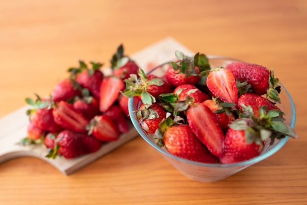 Frisch geschnittene Erdbeeren auf einem Holzschneidebrett und köstliche Erdbeeren in einer Glasschüssel auf Holztisch.