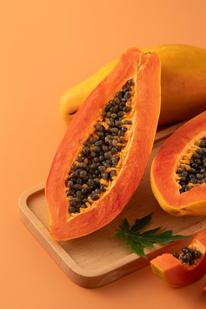 Frisch geschnittene Papayafrüchte auf orangefarbenem Tischhintergrund für tropisches Gourmet-Designkonzept