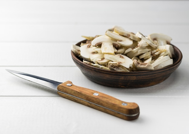Frisch geschnittene Pilze in einer Tonschale und einem Messer auf einem weißen Holztisch