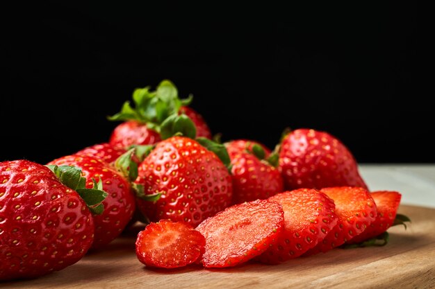 Frisch geschnittene rote erdbeeren auf einem holzbrett mit dunkelheit