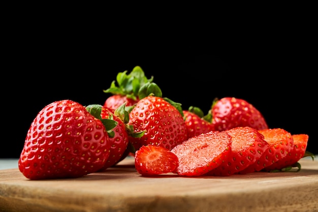 Frisch geschnittene rote Erdbeeren auf einem Holzbrett mit Dunkelheit