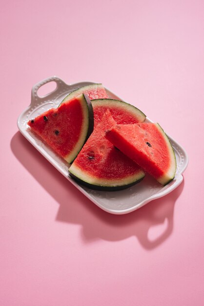 Frisch geschnittene Wassermelone in weißer Schale auf rosa Tisch.