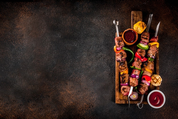 Frisch, hausgemacht auf dem Grill Feuer Fleisch Rindfleisch Schaschlik mit Gemüse und Gewürzen, mit Barbecue-Sauce und Ketchup, auf einem dunklen Hintergrund auf einem hölzernen Schneidebrett über Kopie Raum