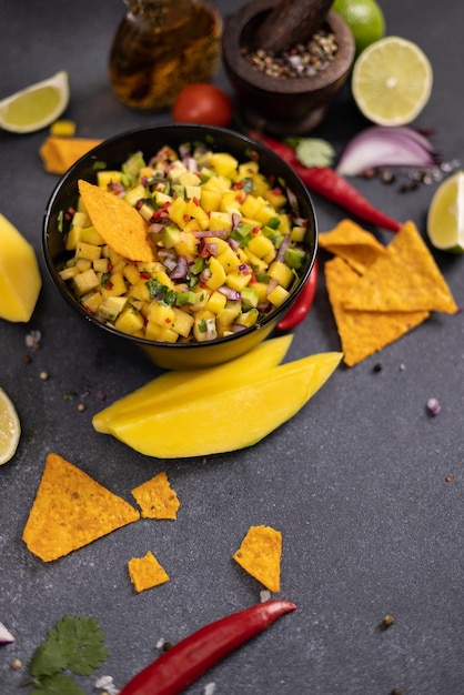 Frisch hergestellte Mango-Salsa in einer schwarzen Keramikschüssel mit Nachoschnitzeln und Zutaten