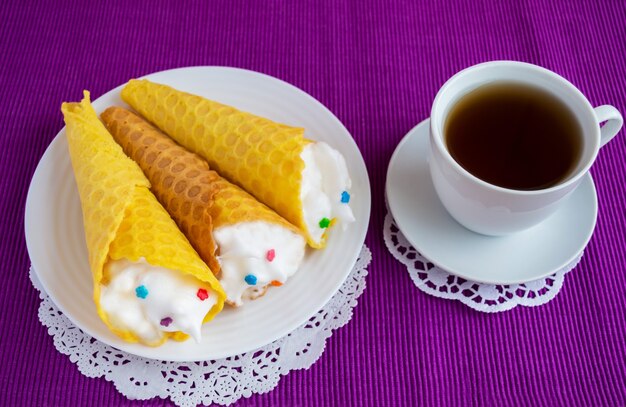 Frisch Honigwaffeln zu einer Tüte mit einer sanften Creme auf einer bunten Serviette und einer Tasse Tee