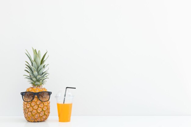 Frische Ananas mit Sonnenbrille neben einem Glas Saft und einem Cocktailstroh auf farbigem Hintergrund