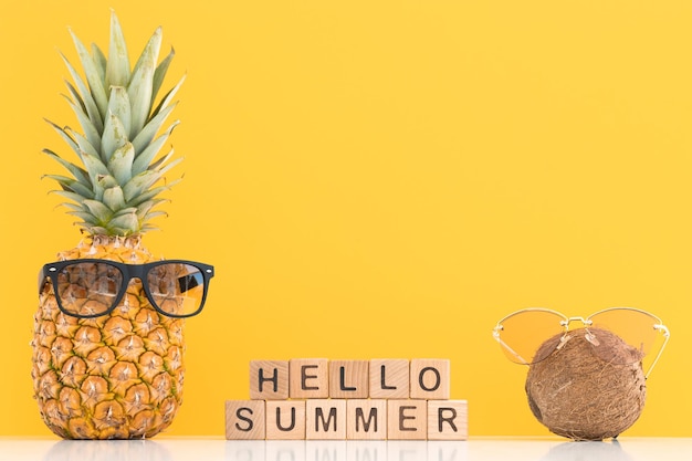 Frische Ananas und Kokosnuss mit Sonnenbrille auf farbigem Hintergrund Hallo Sommer