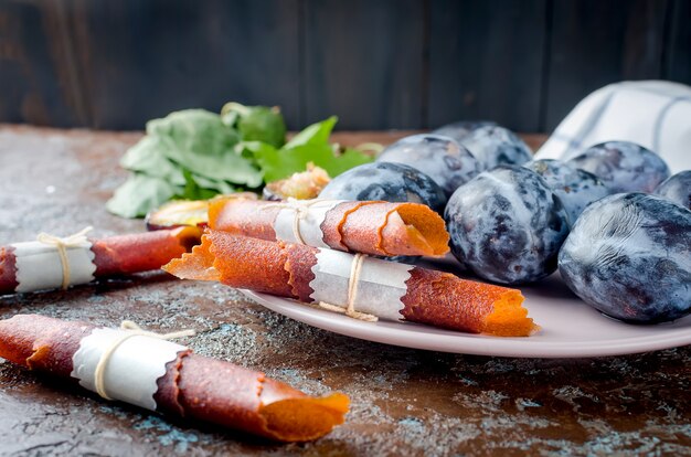 Frische ausgewählte Pflaumen in der keramischen Platte und in der Pflaumenpastille auf dunklem Hintergrund