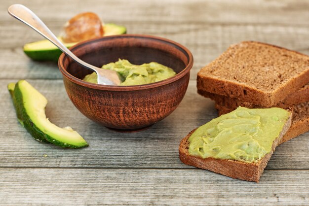 Frische Avocadocreme in der Schüssel, Brotscheiben auf grauem hölzernem Hintergrund