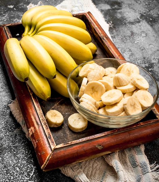 Frische Bananen mit geschnittenen Bananenstücken in einer Schüssel. Auf rustikalem Tisch.