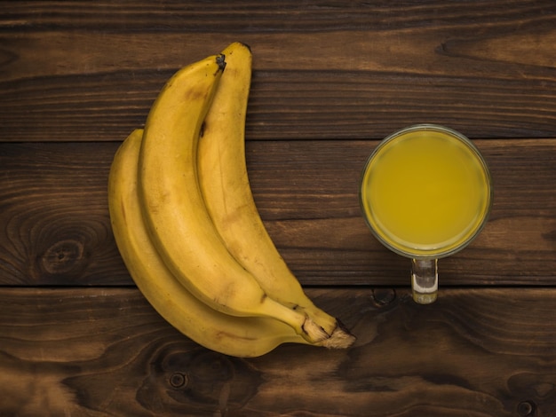 Frische Bananen und ein Glas Bananen-Smoothie auf einem Holztisch Flach lag