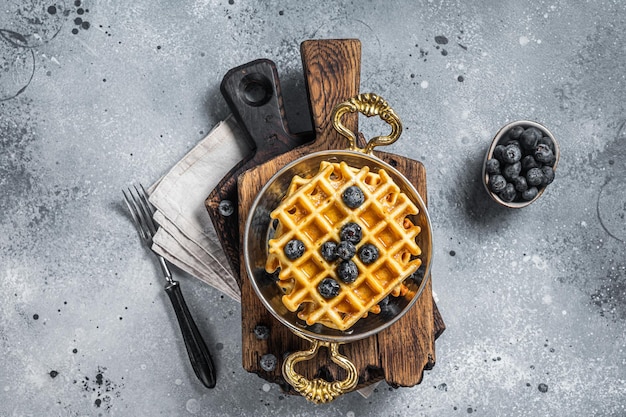 Frische belgische Waffeln mit Blaubeere und Sirup in der Pfanne. Grauer Hintergrund. Ansicht von oben.