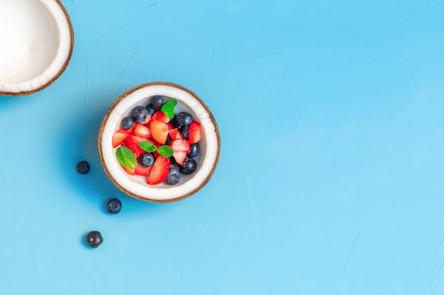 Frische Bio-Beeren in einer Kokosnussschale auf hellblauem Tisch. Gesundes Bio-Esskonzept