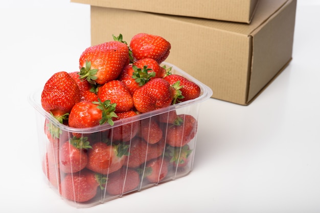 Frische Bio-Erdbeeren in einer Plastikbox und Bastelboxen. Lieferung von Bio-Lebensmitteln. Verpackung von Bio-Erdbeeren. Bastelbox und Bio-Lebensmittel.