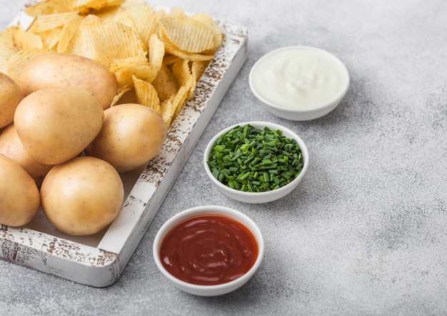 Frische Bio hausgemachte Kartoffelchips Chips mit rohen gelben Kartoffeln in weißer Holzkiste auf hellem Tischhintergrund.