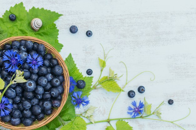 Frische Blaubeeren im Korb mit Blumen- und Blattmuster-Draufsicht. Gesundes Essen auf weißem Tischmodell. Köstliche, süße, saftige und reife Beere mit Platz für Text