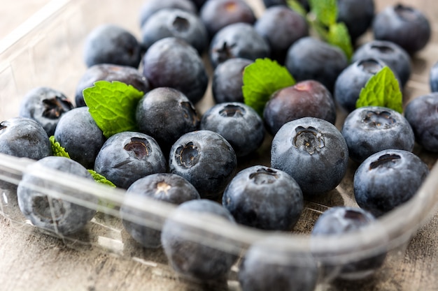 Frische Blaubeeren in Plastikschale auf Holztisch schließen oben