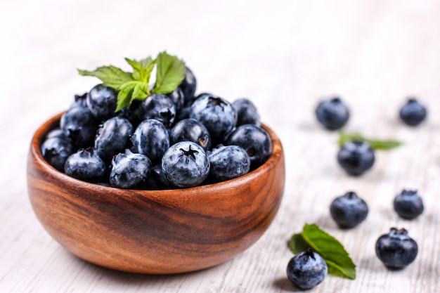 Frische Blaubeeren mit grüner Minze treiben in einer hölzernen Schüssel auf weißer Tabelle Blätter