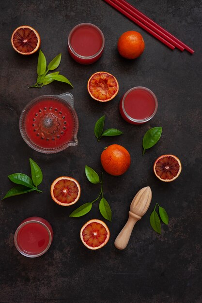 Frische Blutorangefrüchte und -saft mit Holz- und Glassaftpressern auf dunklem Hintergrund