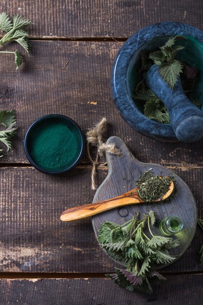 Frische Brennnesselblätter auf Holztisch. Urtica dioica Öl mit Spirulina-Pulver, eine gesunde Ergänzung zur Verbesserung der Gesundheit.