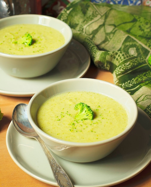 Frische Brokkolicremesuppe auf grauer keramischer Schüssel zwei auf Platte mit Löffel auf Marmorhintergrund.