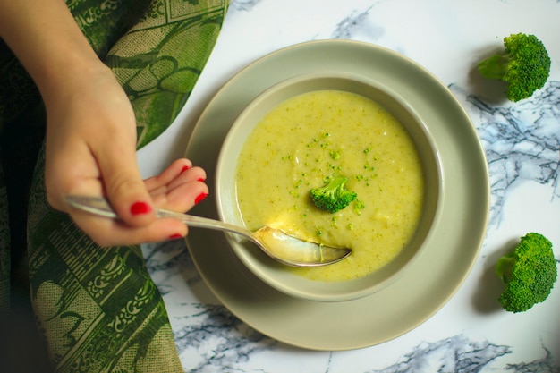 Frische Brokkolicremesuppe auf grauer keramischer Schüssel zwei auf Platte mit Löffel auf Marmorhintergrund.