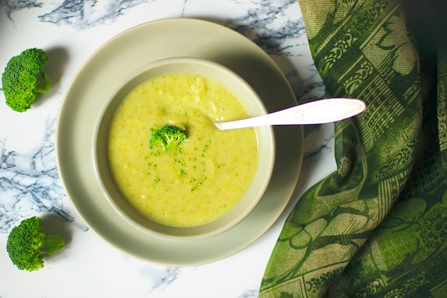 Frische Brokkolicremesuppe auf grauer keramischer Schüssel zwei auf Platte mit Löffel auf Marmorhintergrund.