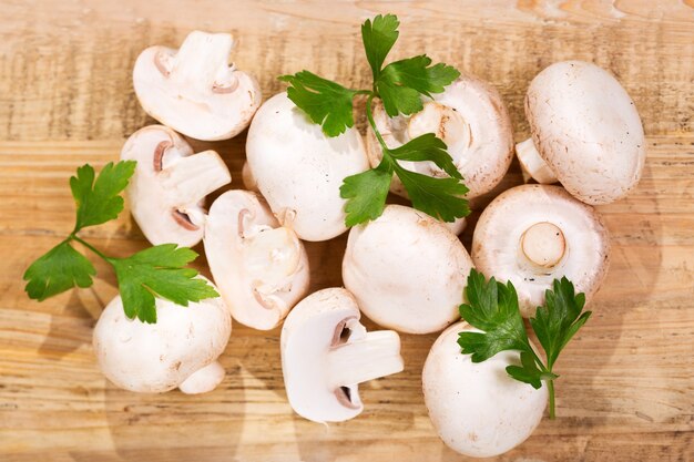 Frische Champignonpilze mit Petersilie auf Holztisch, Draufsicht