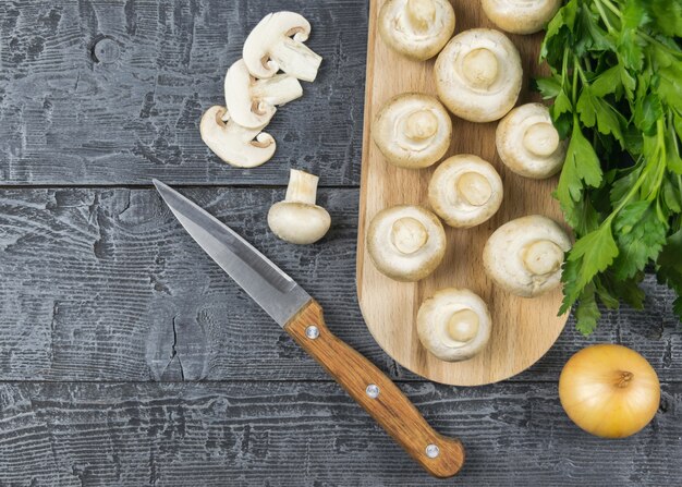 Frische Champignons mit Petersilie und Zwiebel auf Schneidebrett auf rustikalem Tisch