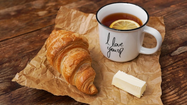 Frische Croissants mit Butter und eine Tasse Tee mit Zitrone auf einem Holztisch Draufsicht Zutaten für ein leckeres Frühstück