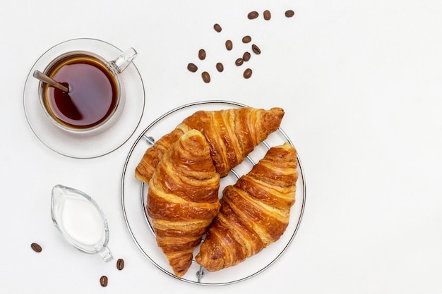 Frische Croissants, Sahne und eine Tasse Kaffee. Platz kopieren. Ansicht von oben. Weißer Hintergrund.