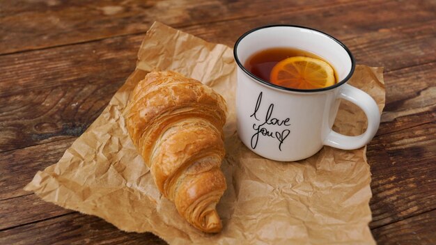 Frische Croissants und eine Tasse Tee mit Zitrone auf einem Holztisch Draufsicht