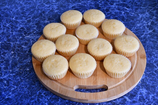 Frische Cupcakes in Papierform auf einem runden Holzbrett. Board mit Cupcakes auf einer blauen Tischplatte.