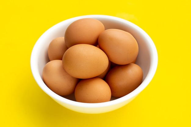 Frische Eier in weißer Schüssel auf gelbem Hintergrund.