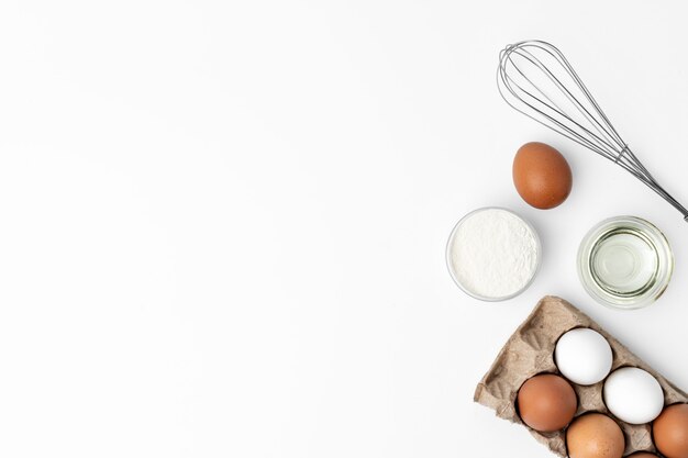 Frische Eier mit Schneebesen auf weißem Hintergrund