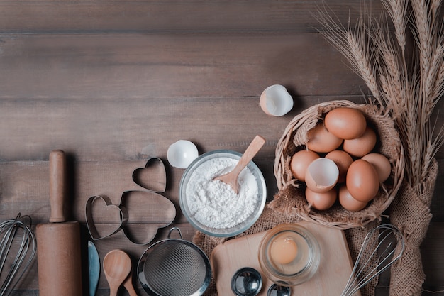 Frische Eier und Kuchenmehl mit Küchenutensilien für Gebäck auf Holz