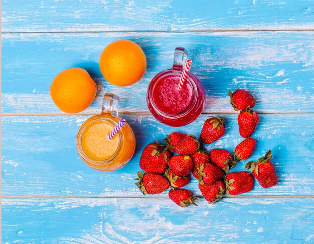 Frische Erdbeer- und Orangencocktails mit Früchten auf einer rustikalen Holzwand.