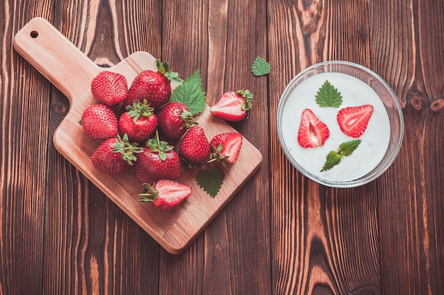 Frische Erdbeeren auf einem hölzernen Brett und einem Joghurt mit Scheiben von Erdbeeren in einer Platte auf einem Holztisch