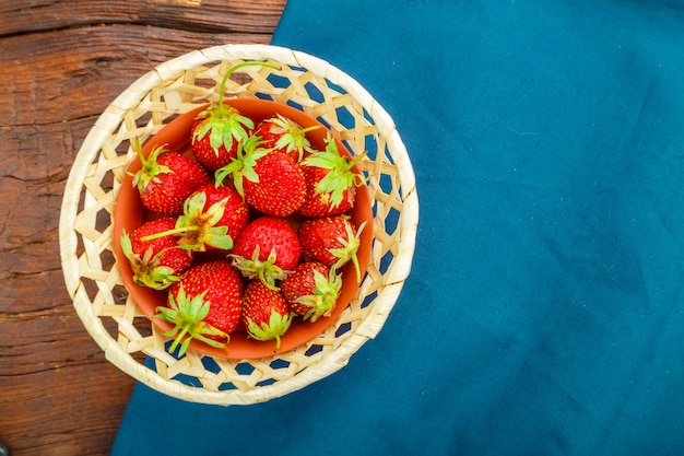 Frische Erdbeeren in einem Korbteller auf einer blauen Serviette auf einer Holzoberfläche