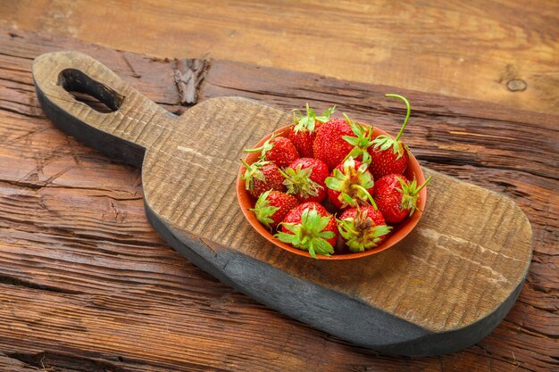 Frische Erdbeeren in einem Teller auf einem Holzbrett auf einem hölzernen Hintergrund. Horizontales Foto